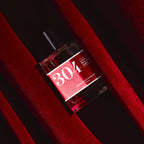 304 Cumin Parfüm – klares Glasfläschchen 100ml, rotes Etikett, schwarzer Verschluss, roter Samthintergrund – Parfum