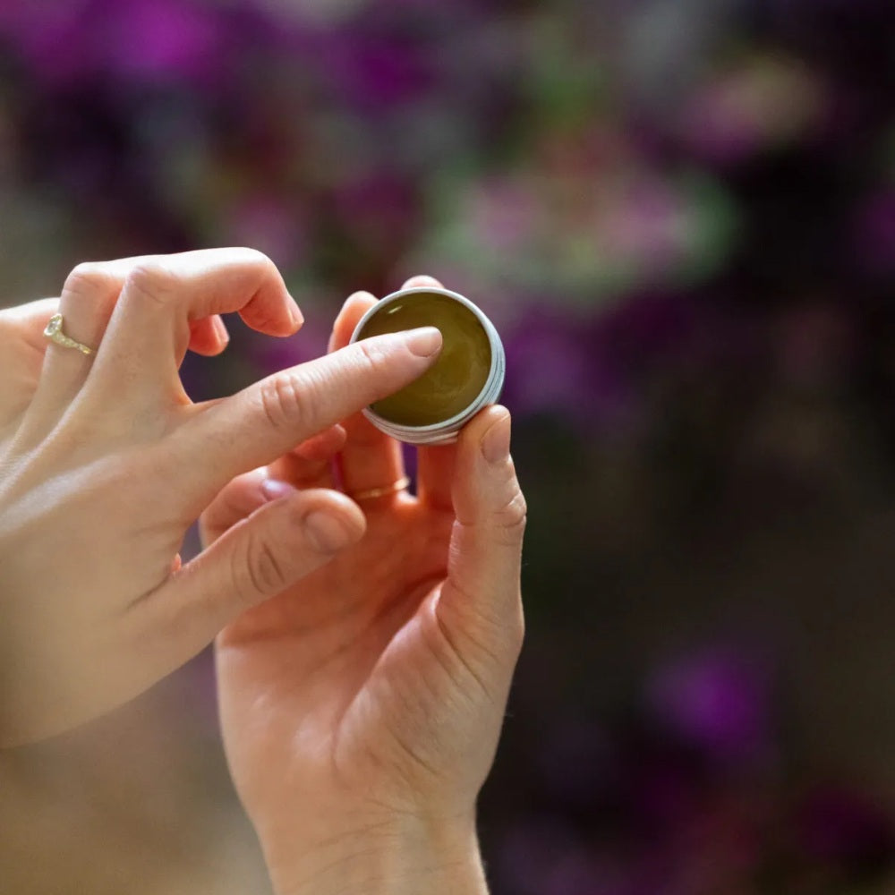 Glow + Repair Lip Balm – kleiner Metallbehälter, grüne Textur, lila unscharfer Hintergrund – Lippenpflege