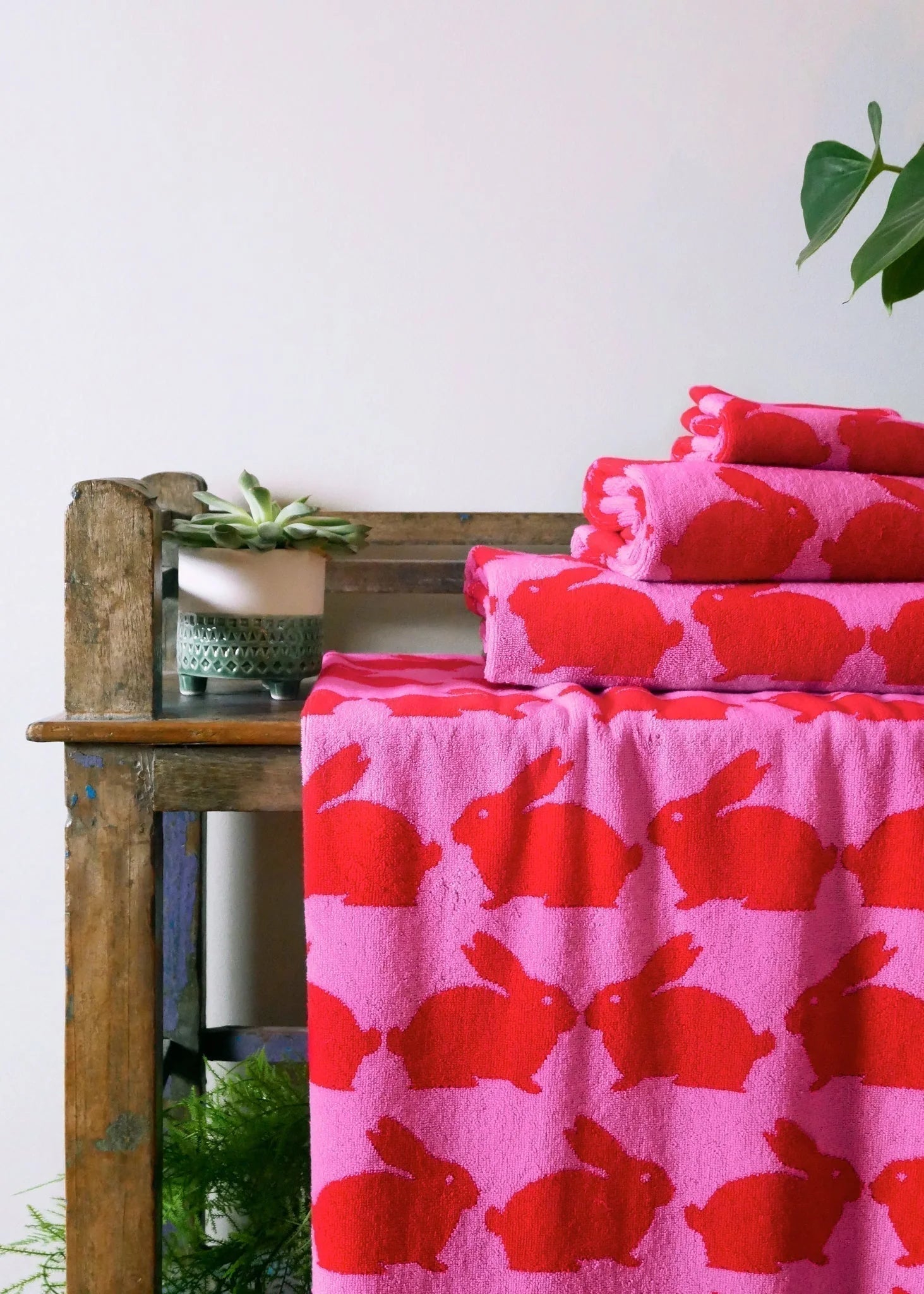 Kissing Rabbits Bio-Baumwoll-Strandtuch – pink mit roten Hasen, auf Holzbank, weißer Hintergrund – Strandaccessoires