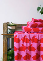 Kissing Rabbits Organic Cotton Bath Towel – pink with red bunnies, on wooden bench, white background – bath towels