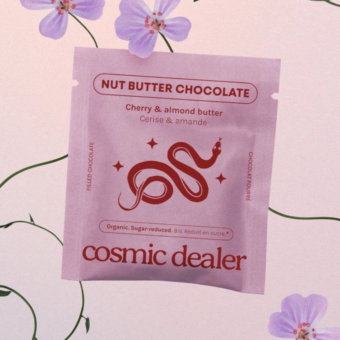 Cosmic Dealer Nut Butter Chocolate – lila Beutel mit Kirsch-Mandel-Butter, rosafarbener Hintergrund mit Blumen – Snack