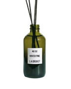 L:A Bruket No. 332 Winter Pine – green glass bottle with rattan reeds, white label on white background – room fragrance