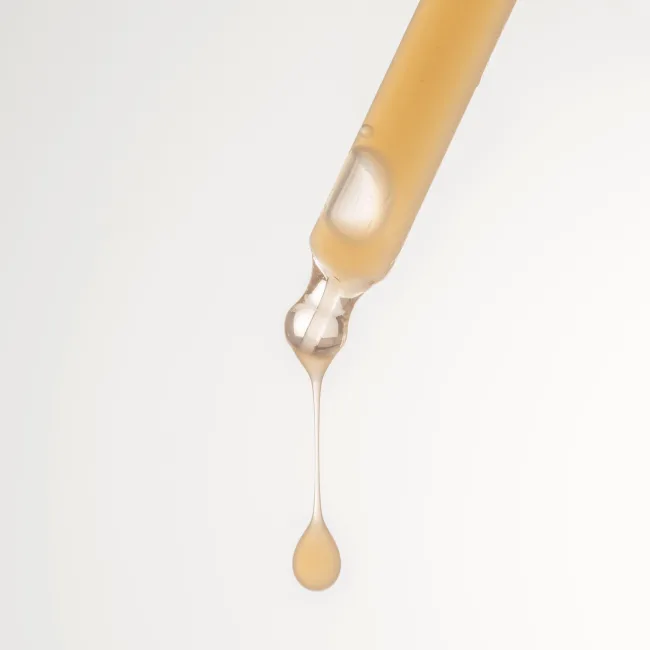 Hydrating Serum Plus: goldfarbene Flüssigkeit an einer Pipette vor weißem Hintergrund, Hautpflege.
