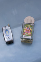 Maison Matine Faire Le Mur Eau de Parfum – klares Glasflakon mit farbenfrohem Etikett, runder Steinverschluss, blauer Hintergrund – Parfüm