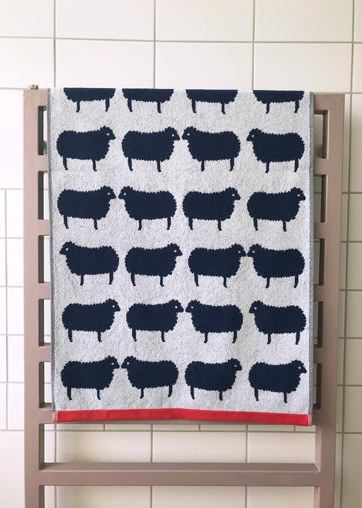 Sheep Organic Cotton Badetuch – hellgrau mit schwarzen Schafen, roter Saum, auf Heizkörper – Badetücher