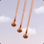 Three copper tongue cleaners with shell heads against purple sky – tongue care