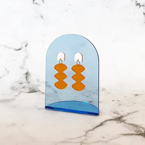 Spectral Orange Ohrringe – orangefarbene geometrische Formen auf blauem Acrylhalter, Marmorhintergrund – Schmuck