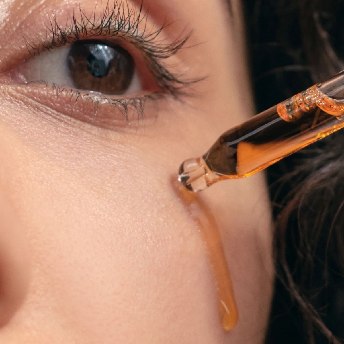 Bakuchiol Anti-ageing Oil – golden serum drips from dropper onto skin, dark background – skin care