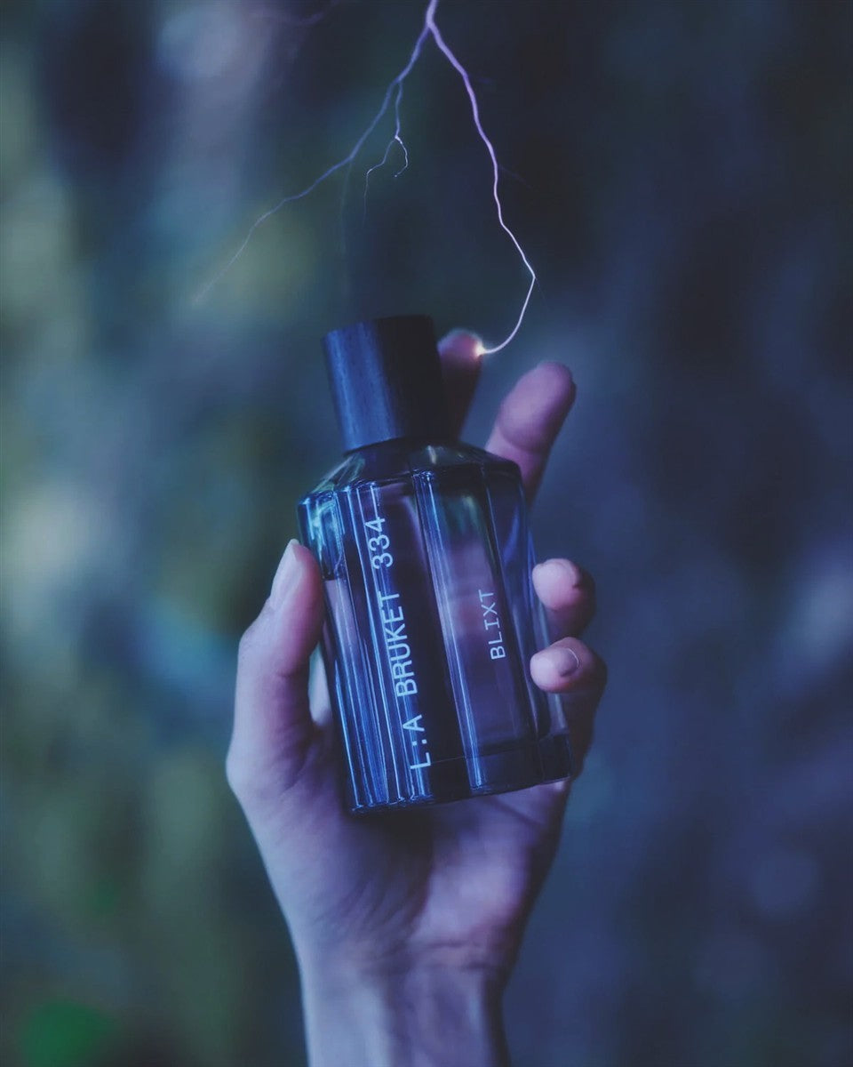 L:A BRUKET No. 334 Blixt Eau de Parfum – dunkelblaue Glasflasche mit schwarzen Deckel, blauer Hintergrund – Parfüm