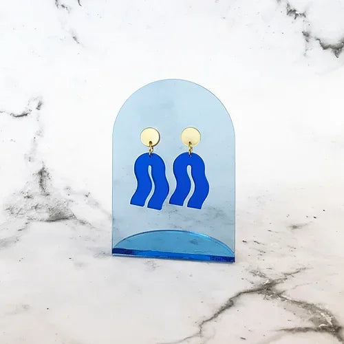 Spectral Blue Ohrringe – blaue Acrylform mit goldener Fassung, auf blauem Acrylständer, Marmorhintergrund – Schmuck