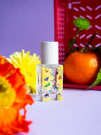 Poom Poom Eau de Parfum – quadratische Glasflasche mit bunten Motiven, weißer Sprühkopf, lila Hintergrund – Parfüm