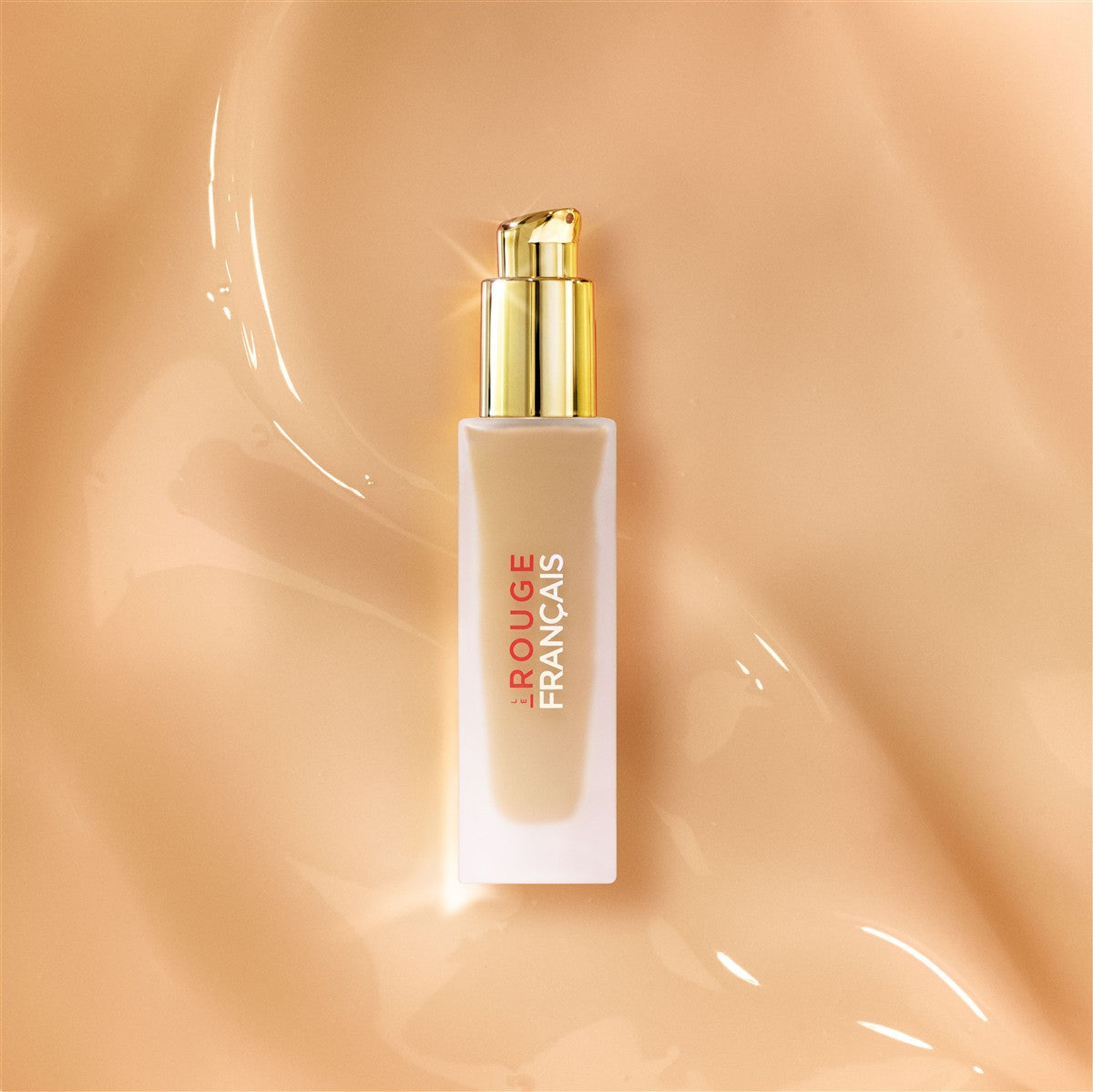 Le Rouge Français Le Fluide de Teint – cremefarbene Flasche mit goldener Pumpe, beige Hintergrund – Make-up