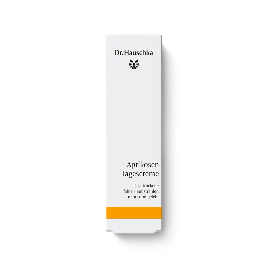 Dr. Hauschka Aprikosen Tagescreme – weiße Kartonverpackung mit orangefarbenem Streifen, weißer Hintergrund – Hautpflege