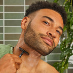 Perfect Glide Safety Razor Black – Mann rasiert sich mit schwarzem Sicherheitsrasierer, grüne Fliesen und Pflanze im Hintergrund – Rasur
