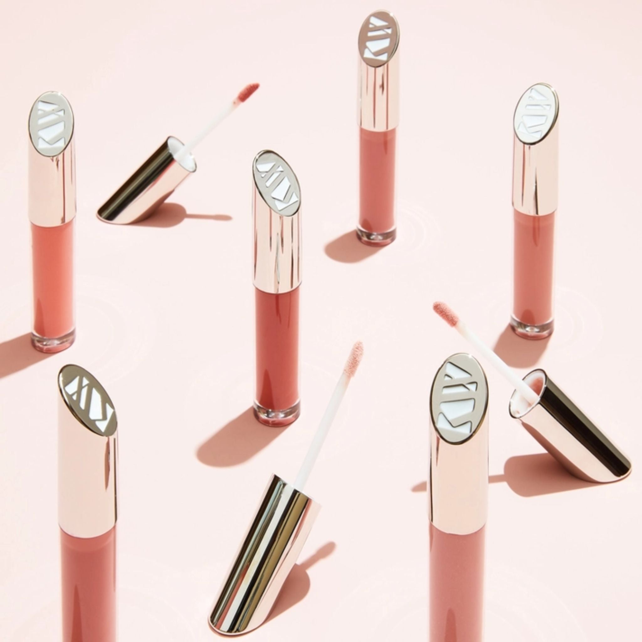 Lip Gloss Courage in pink glass tubes with silver caps on a light pink background for glossy lips.
