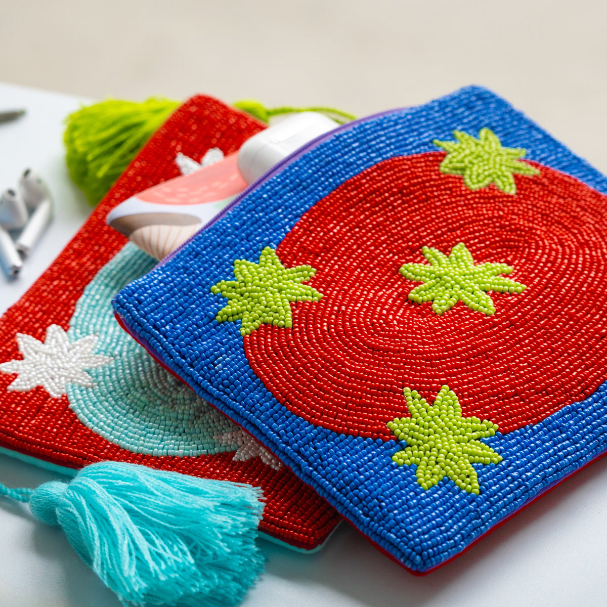 Clutch Galaxy Red, zwei perlenbestickte Taschen in Blau und Rot mit grünen Sternen und Quasten auf weißem Untergrund.