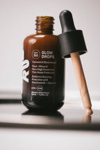 Glow Drops SPF 50 brown glass bottle with dropper, in a bathroom