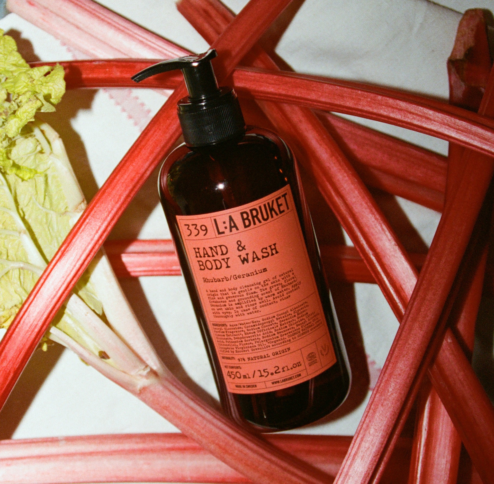L:A Bruket No. 339 Hand & Body Wash, brown bottle with rhubarb red label, surrounded by rhubarbs