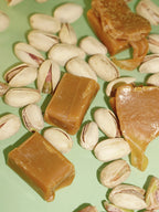 Ingredients of Caramel & Pistachio Nourishing Hand Cream: caramel pieces and pistachios on green background, skin care.