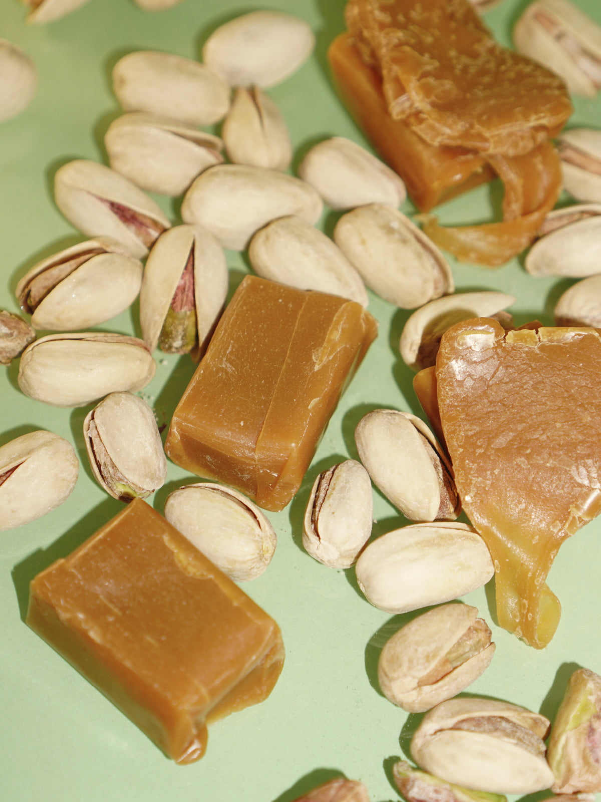 Ingredients of Caramel & Pistachio Nourishing Hand Cream: caramel pieces and pistachios on green background, skin care.