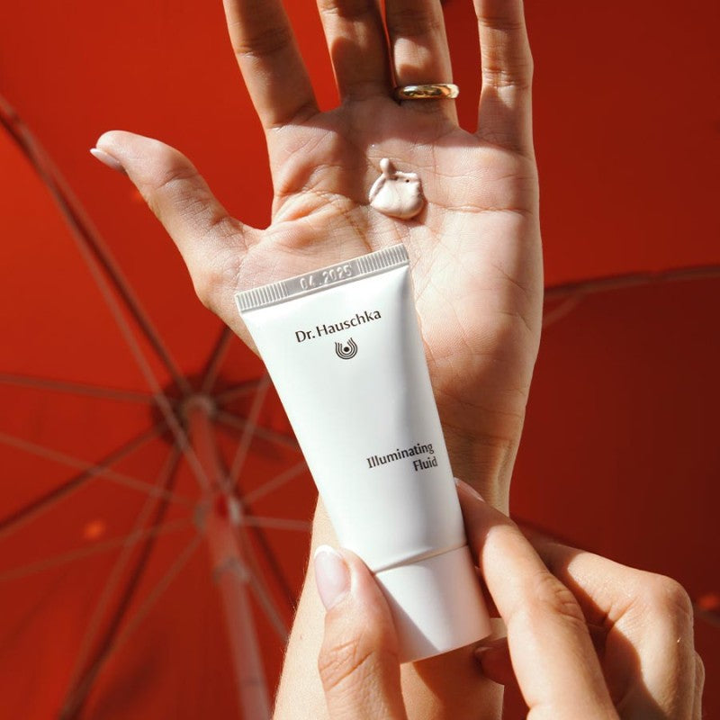 Dr. Hauschka Illuminating Fluid – weiße Tube, silberner Verschluss, roter Hintergrund – Gesichtspflege