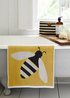 Buzzy Bee Organic Cotton Washcloth – yellow with bee design, white border, on bathtub – skin care