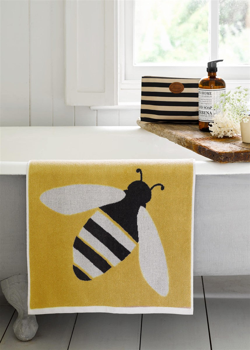 Buzzy Bee Bio-Baumwollwaschlappen – gelb mit Bienenmotiv, weißer Rand, auf Badewanne – Hautpflege