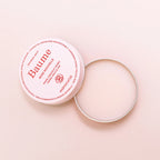 Baume Rose Nouvelle in a pink tin with an open silver lid on a pink background, skin care