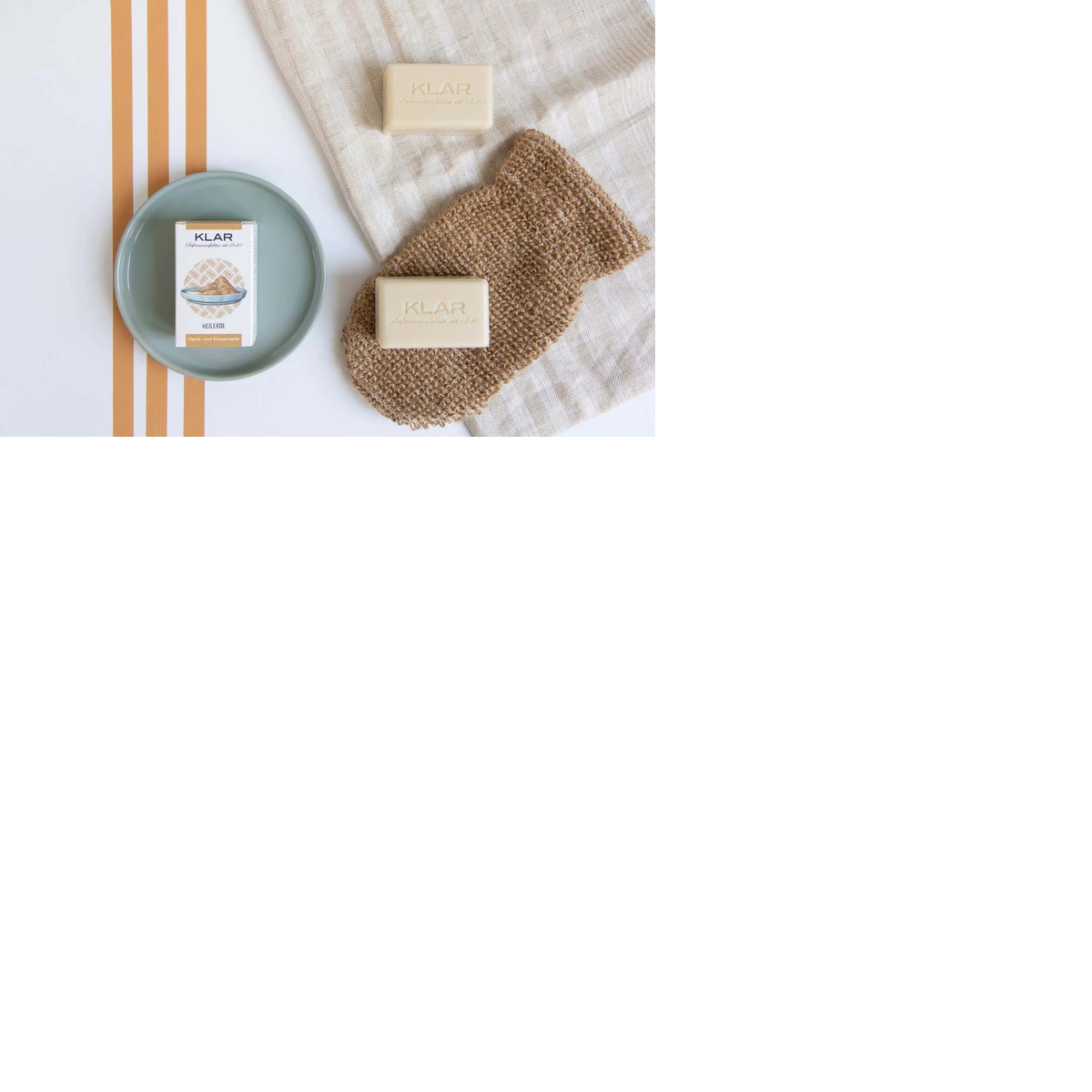 KLAR Heilerde Seife – cremefarbene Seifenstücke, Verpackung auf grünem Teller, beige Tuch – Hautpflege
