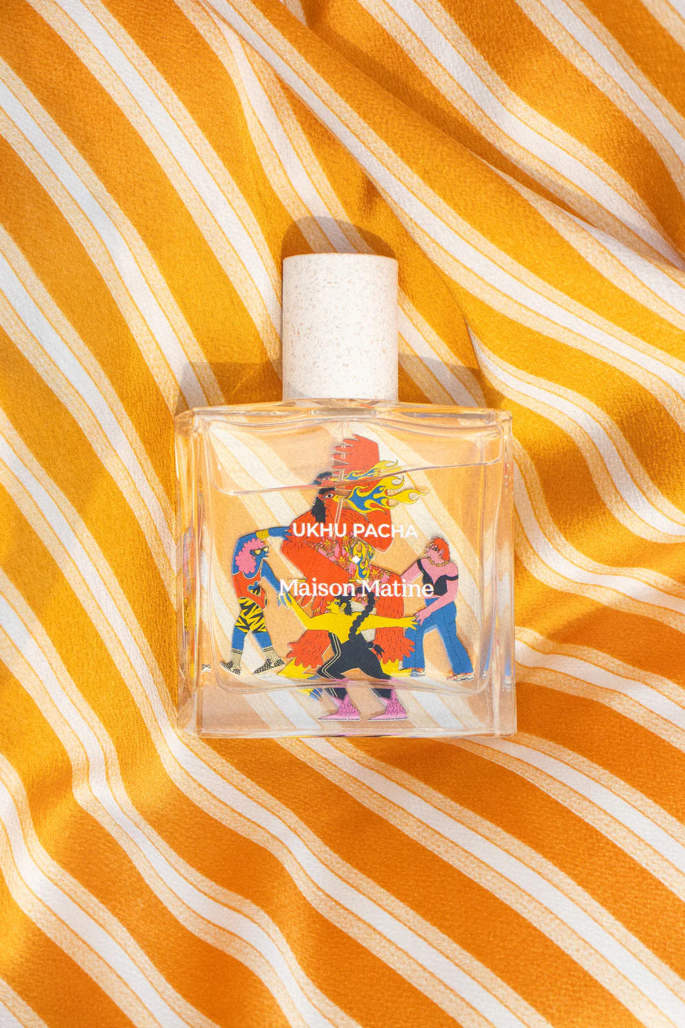 Ukhu Pacha Eau de Parfum – klares Glasflakon mit weißem Sprühkopf, orangefarben-weißer Streifenhintergrund – Parfüm