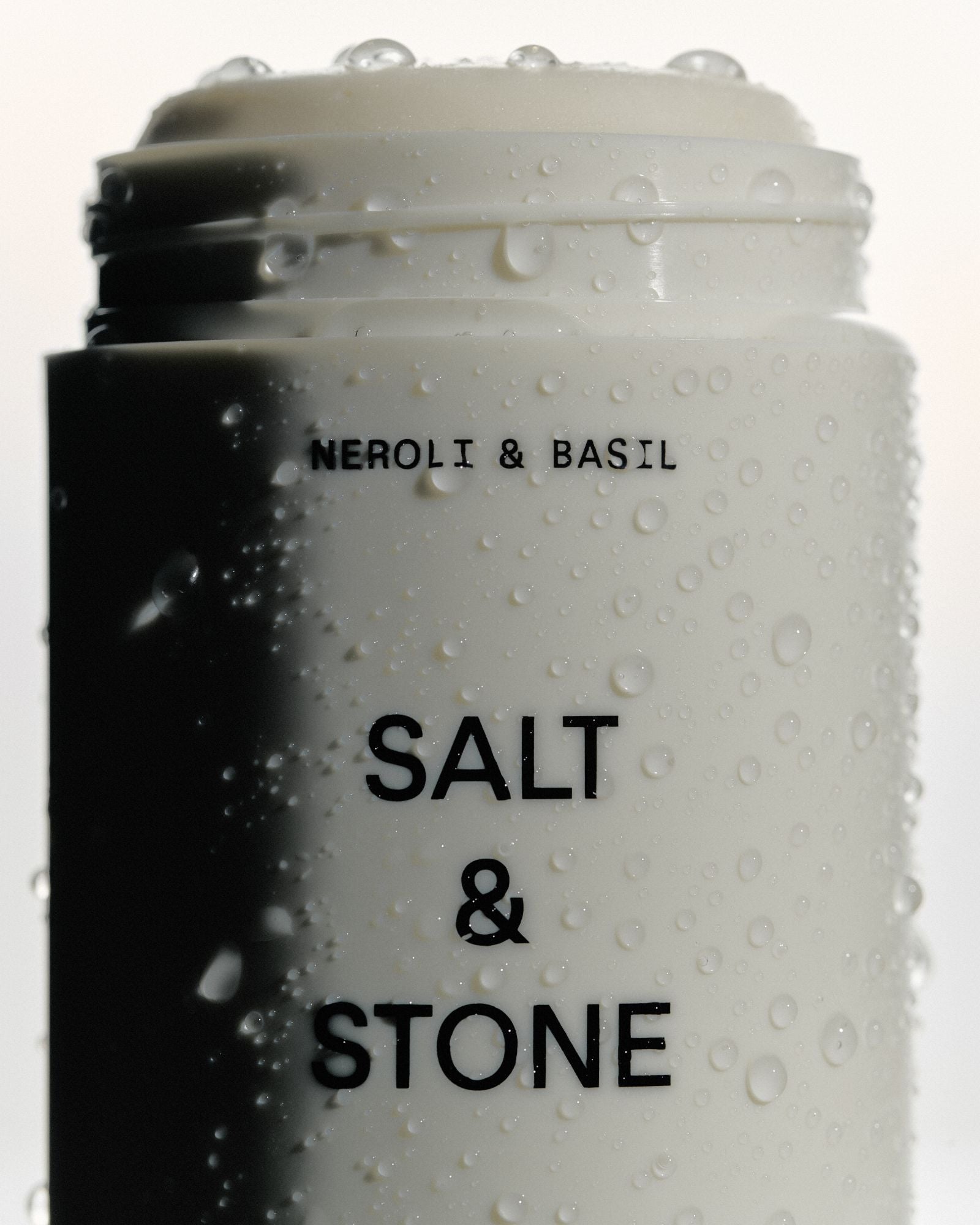 Salt & Stone Neroli & Basil Deo Extra Strength – weißer Stift mit schwarzem Deckel, wasserbedeckt, weißer Hintergrund – Deo