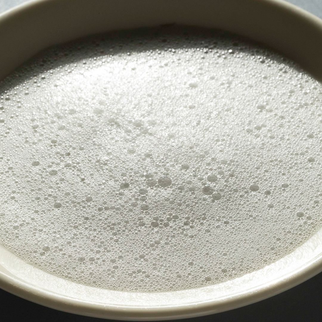 Unica Smoothiebody Bath – cremiger Schaum in weißer Schale, dunkler Hintergrund – Körperpflege