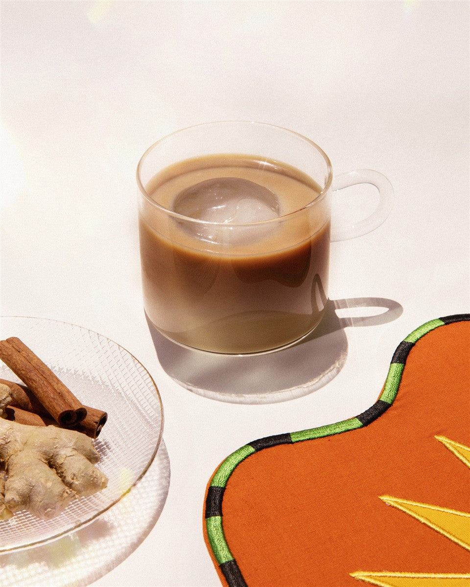 Chai Koffee – durchsichtige Tasse mit braunem Getränk, Eiswürfel, Zimtstangen und Ingwer im Hintergrund – Getränke