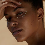 La Crème Réparatrice Regard – Augencreme auf dunkler Haut, beige Hintergrund – Augenpflege