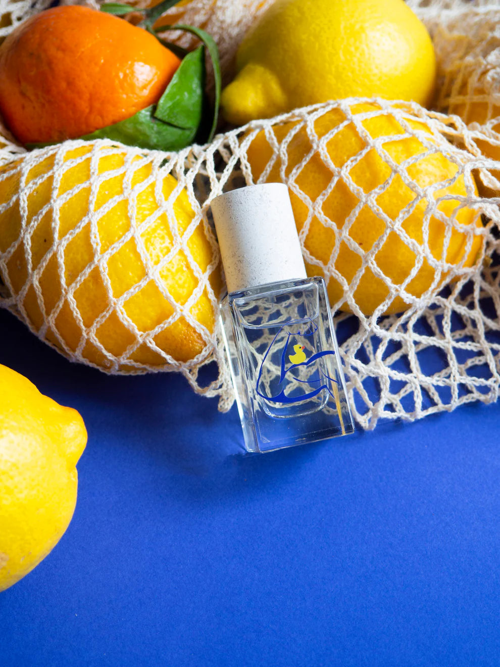 Esprit de Contradiction Eau de Parfum – klares Glasfläschchen mit weißem Sprühkopf, blauer Hintergrund, Zitrusfrüchte – Parfüm