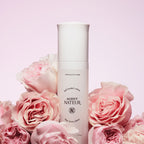Agent Nateur holi (water) crème: Weiße Flasche mit weißem Verschluss vor rosa Rosen, Hautpflege.