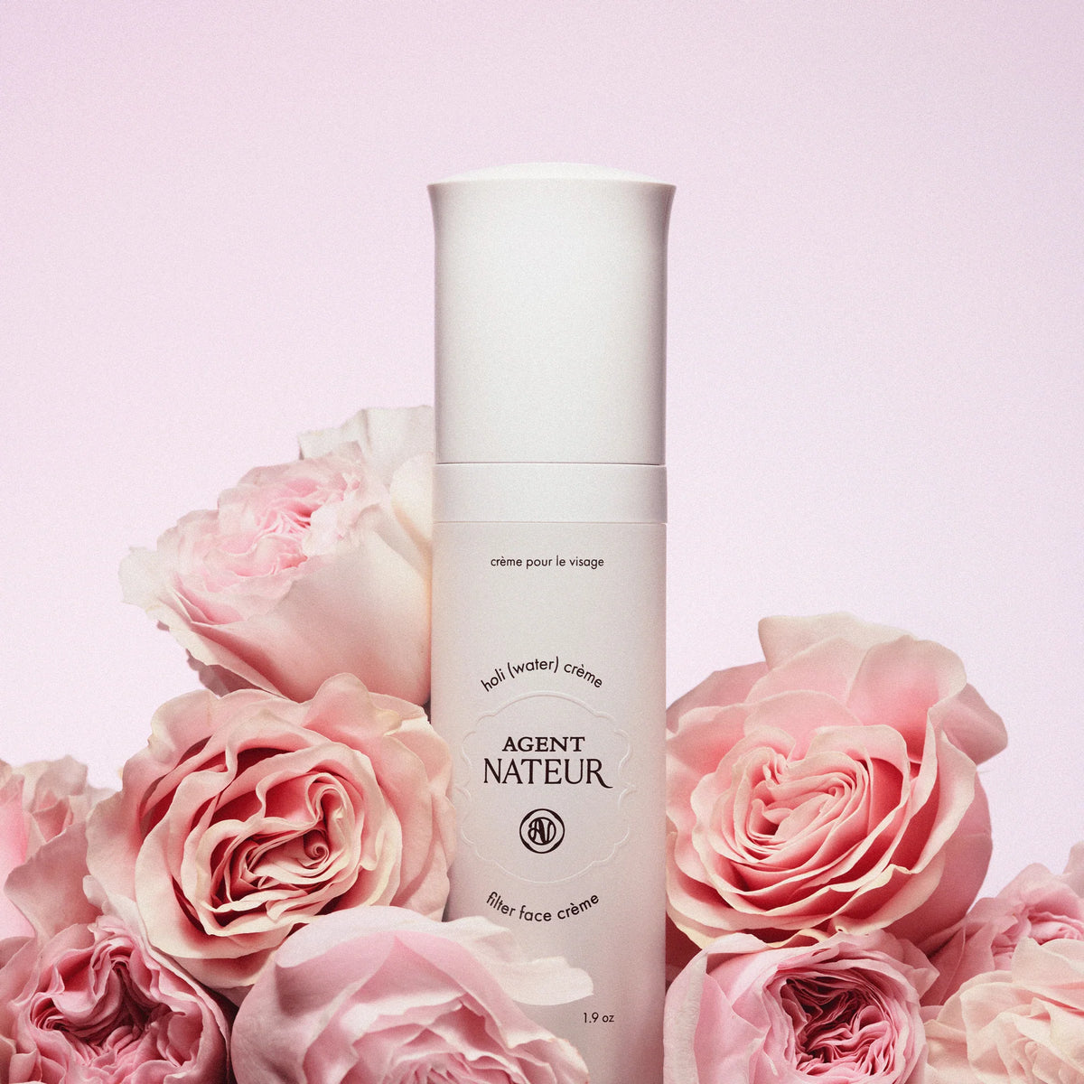 Agent Nateur holi (water) crème: Weiße Flasche mit weißem Verschluss vor rosa Rosen, Hautpflege.