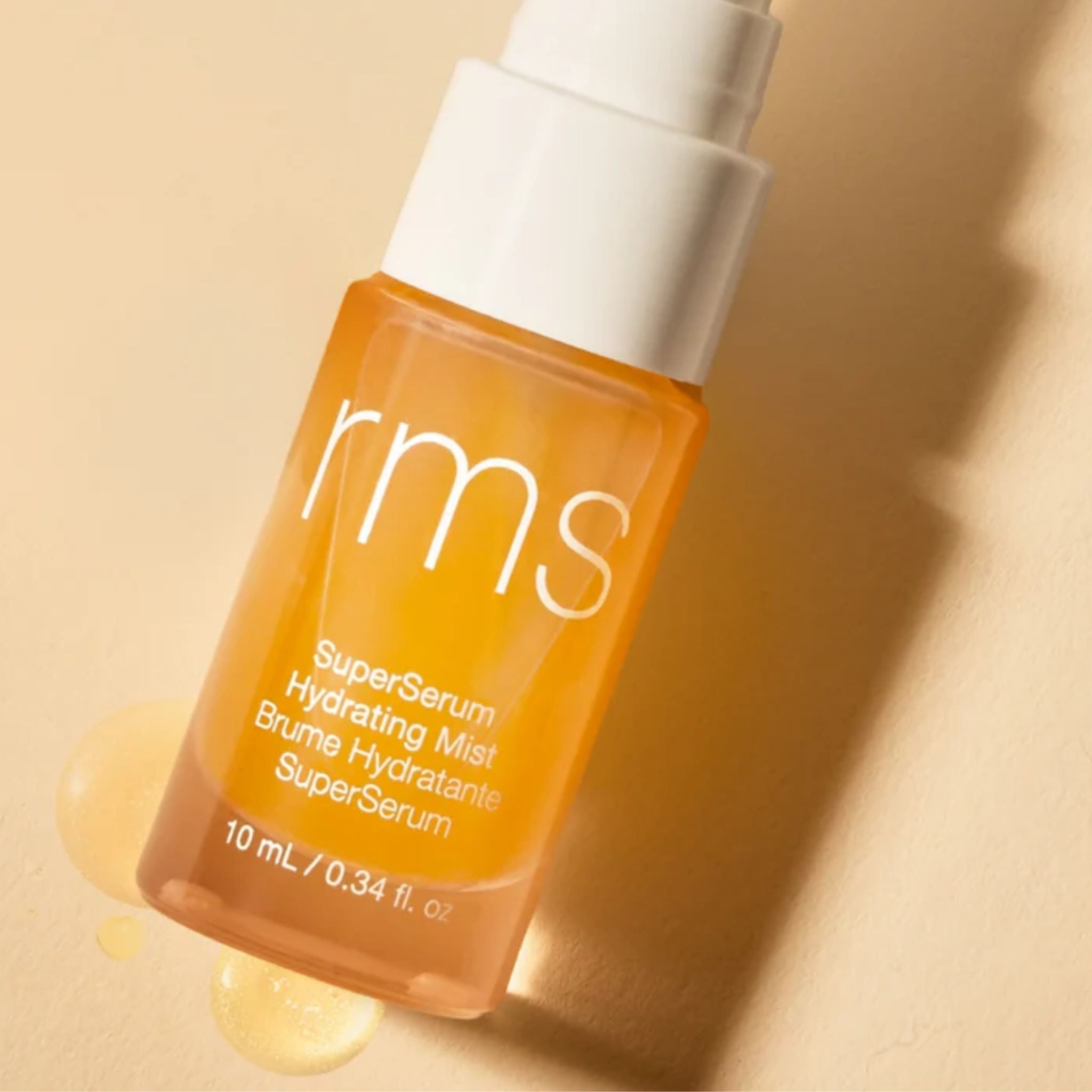 RMS Beauty SuperSerum Hydrating Mist Sprühflasche in Orange mit weißem Verschluss auf beigem Grund, Hautpflege