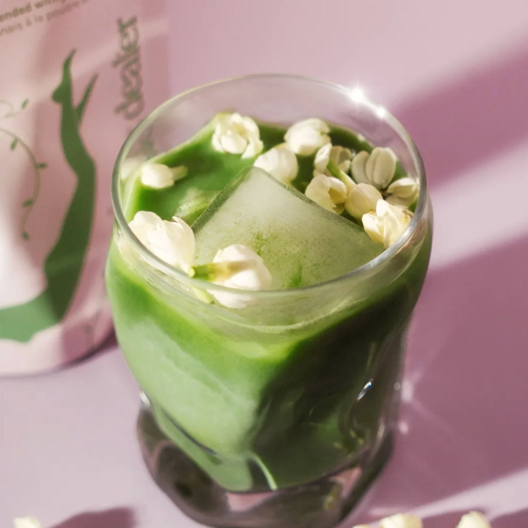 Jasmine Matcha in a glass on a pink background, green drink with blossoms