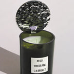 L:A Bruket Candle Reflektor, grünes Glasgefäß mit silbernem Metalldeckel vor hellem Hintergrund, Duftkerze.