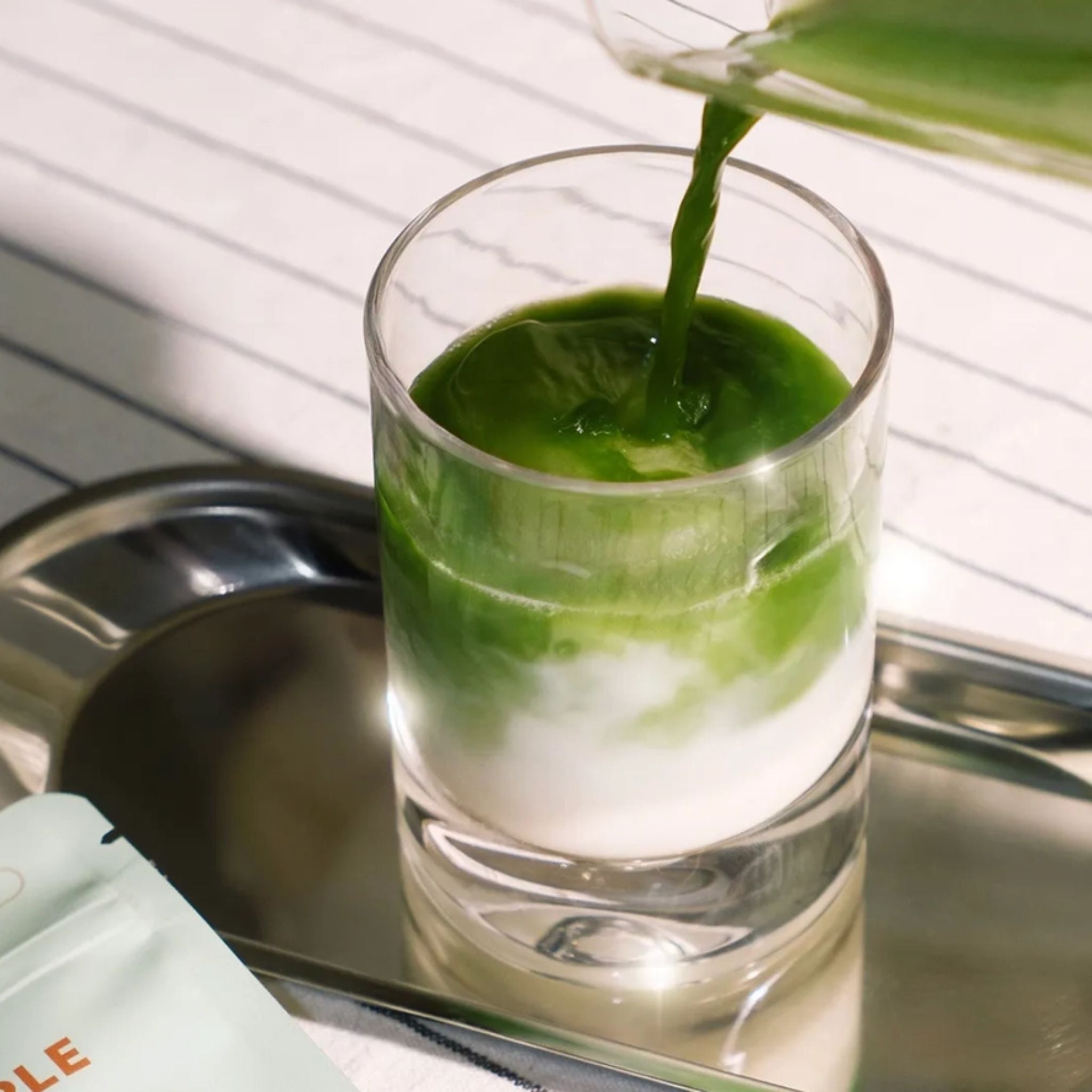 Spiced Maple Matcha Getränk wird in ein Glas gegossen, grün und weiß auf silbernem Tablett, Wellness-Getränk