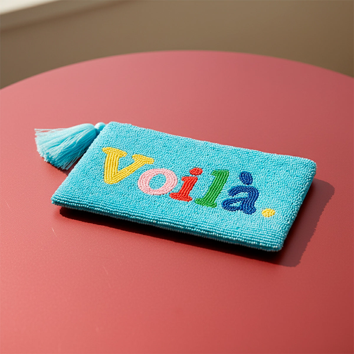 Voilà Clutch, light blue beaded clutch with colourful lettering on a reddish background.