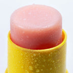XOXO Lippenbalsam, Nahaufnahme des rosa Balsam-Sticks in einem gelben Kunststoffbehälter mit Wassertropfen auf der Oberfläche.