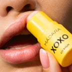 Mádara XOXO Lippenbalsam: Ein gelber Lippenstift-Stick wird auf die Lippen aufgetragen.
